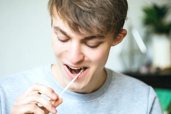 Ein junger potenzieller Spender sitzt entspannt zu Hause und registriert sich als Spender. Dafür streicht er mit dem Wattestäbchen an der Wangeninnenseite entlang.