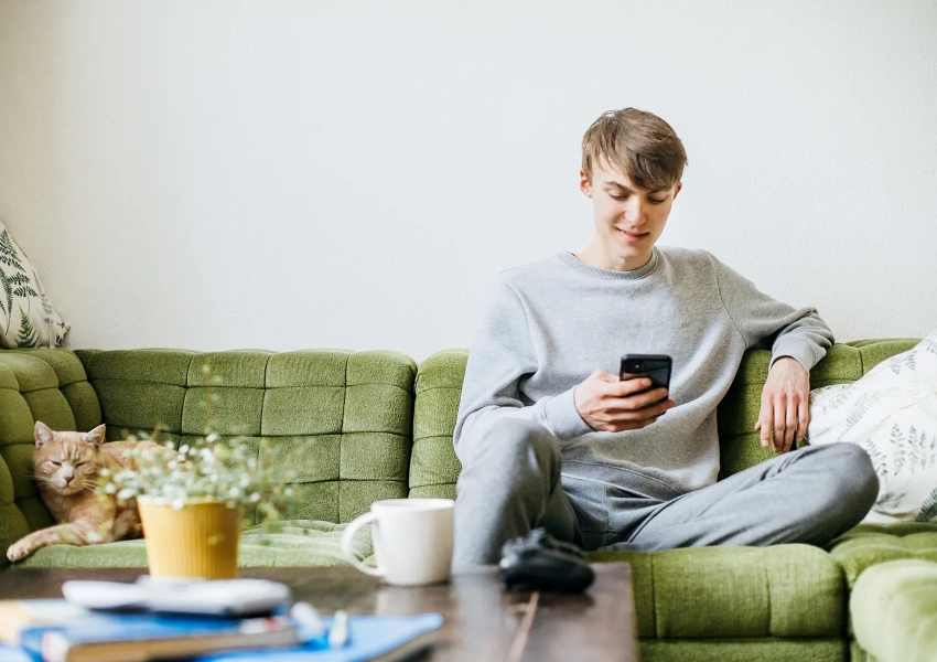 Ein junger potenzieller Spender sitzt entspannt zu Hause auf der Couch und registriert sich online am Handy.