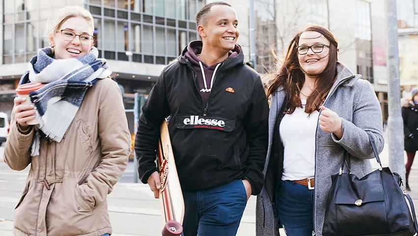 Drei junge Knochenmarkspender laufen lachend über die Straße, sie vereint das gemeinsame Erlebnis der Spende.