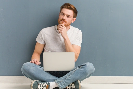 Ein junger potenzieller Spender sitzt entspannt zu Hause mit dem Laptop auf dem Schoss und schaut fragend. Er überlegt: Was ist eigentlich Blutkrebs. 