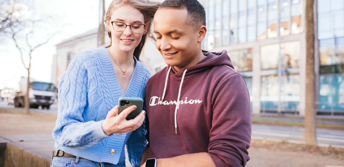 Zwei junge Knochenmarkspender schauen gespannt auf ein Handy und planen eine Aktion gemeinsam gegen Blutkrebs.