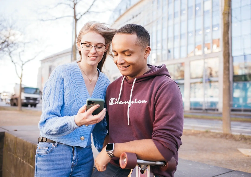 Zwei junge Knochenmarkspender schauen gespannt auf ein Handy und planen eine Aktion gemeinsam gegen Blutkrebs.