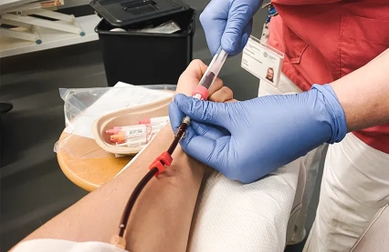 Detailaufnahme einer medizinischen Fachkraft, die professionell eine Nadel in Johannes Arm einführt, um eine Blutprobe abzunehmen