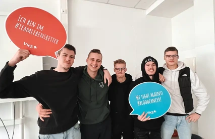 Engagierte Schüler des OSZ Kfz Berlin posieren gemeinsam beim VKS-Registrierungsevent, wobei sie Schilder mit Botschaften zur Bekämpfung von Blutkrebs hochhalten und ihr Engagement für die Sache zum Ausdruck bringen