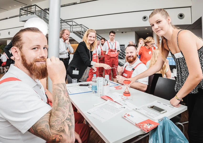 Die Mitarbeiter und Mitarbeiterinnen eines Autoherstellers sitzen zusammen und registrieren. Dabei freuen sie sich in das Team der Lebensretter zukommen. 