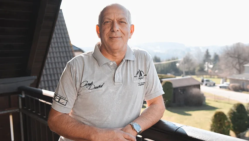 Dieter Langner steht mit Zuversicht auf einem Balkon, umgeben von einer malerischen Landschaft, ein Sinnbild für Hoffnung und das Engagement im Kampf gegen Blutkrebs