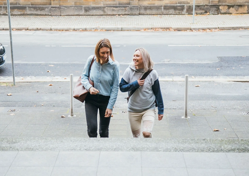 Juliane und Michelle vom VKS Team kommen gemeinsam ins Office. Sie unterhalten sich und lachen zusammen.