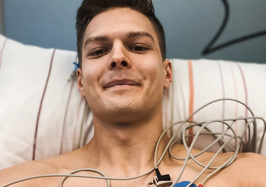 Ein nach der Knochenmarkspende entspannter Johannes liegt im Krankenhausbett, umgeben von medizinischen Überwachungsgeräten, die seine Vitalfunktionen während des Regenerationsprozesses nach der Spende überwachen