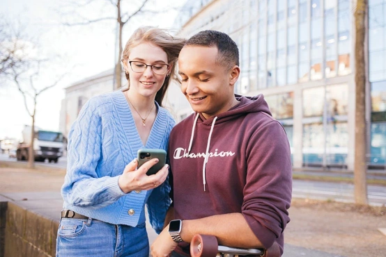 Zwei junge Knochenmarkspender schauen gespannt auf ein Handy und planen eine Aktion gemeinsam gegen Blutkrebs.